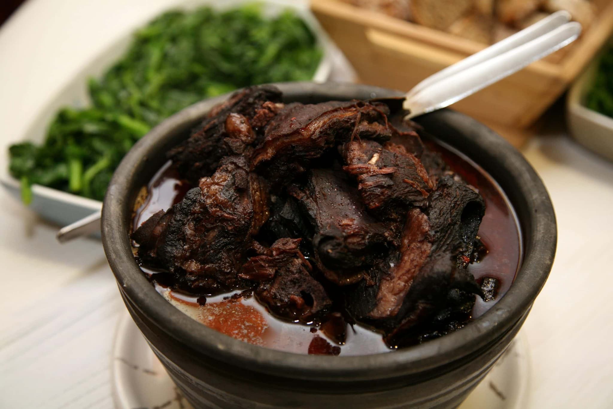 A rustic clay pot filled with tender, dark-braised goat meat in a rich red wine sauce, garnished with fresh parsley and served alongside crusty Portuguese bread