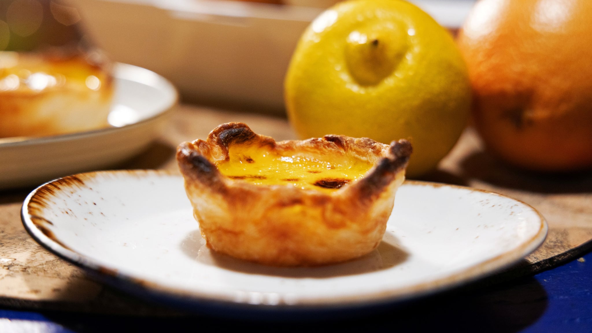 Golden pastéis de nata with caramelized tops arranged on a traditional Portuguese ceramic plate, with the historic Jerónimos Monastery visible in the background