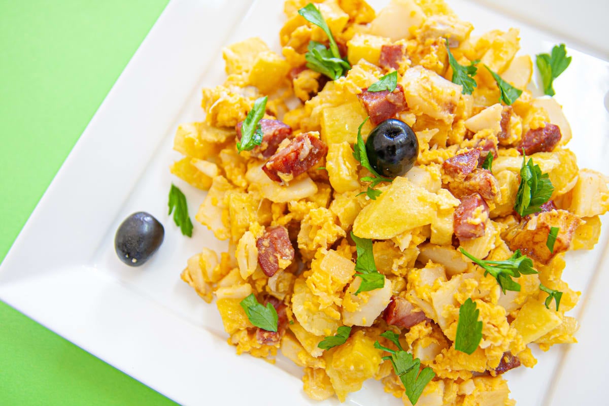A golden, creamy mixture of shredded salt cod, matchstick potatoes, and scrambled eggs garnished with black olives and fresh parsley in a traditional Portuguese serving dish