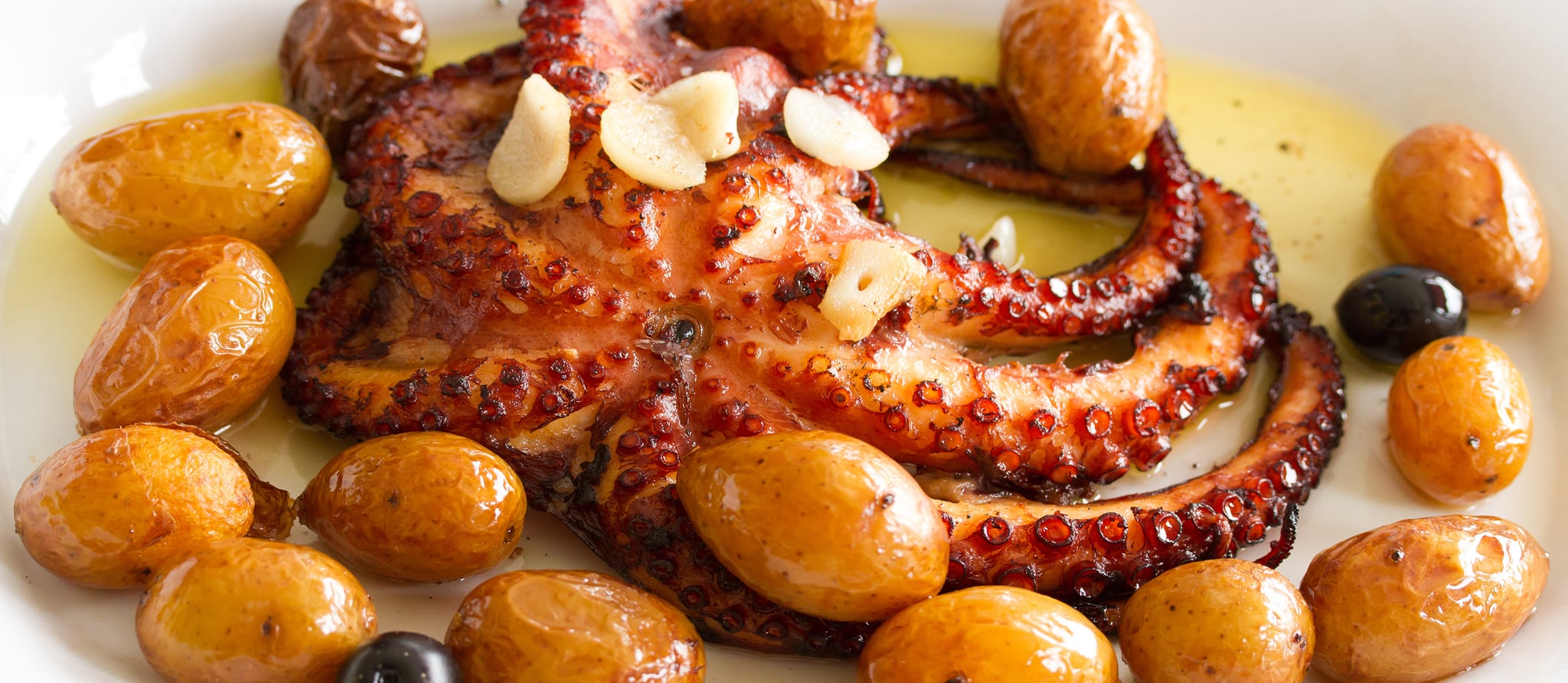 Tender roasted octopus tentacles and golden crispy potatoes glistening with olive oil and garlic, garnished with fresh parsley on a rustic serving platter