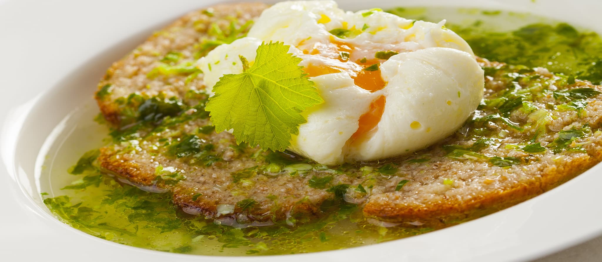 A rustic bowl of Açorda Alentejana showing thick, porridge-like bread soup with green flecks of cilantro, topped with a poached egg and drizzled with golden olive oil