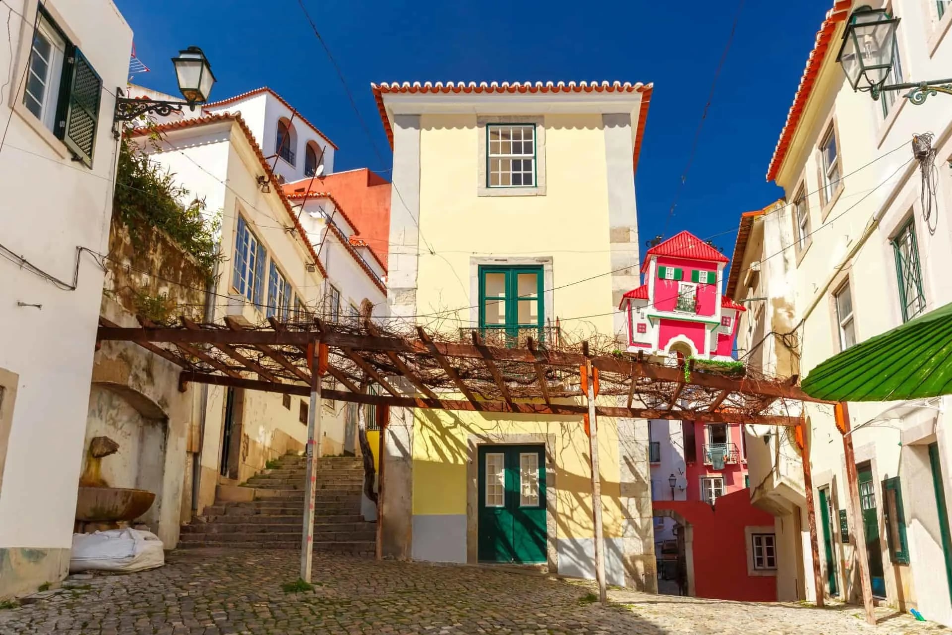 Narrow cobblestone street in Alfama neighbourhood with traditional Portuguese restaurant terraces, grilled sardines on outdoor grills, and locals dining at small tables under colorful awnings