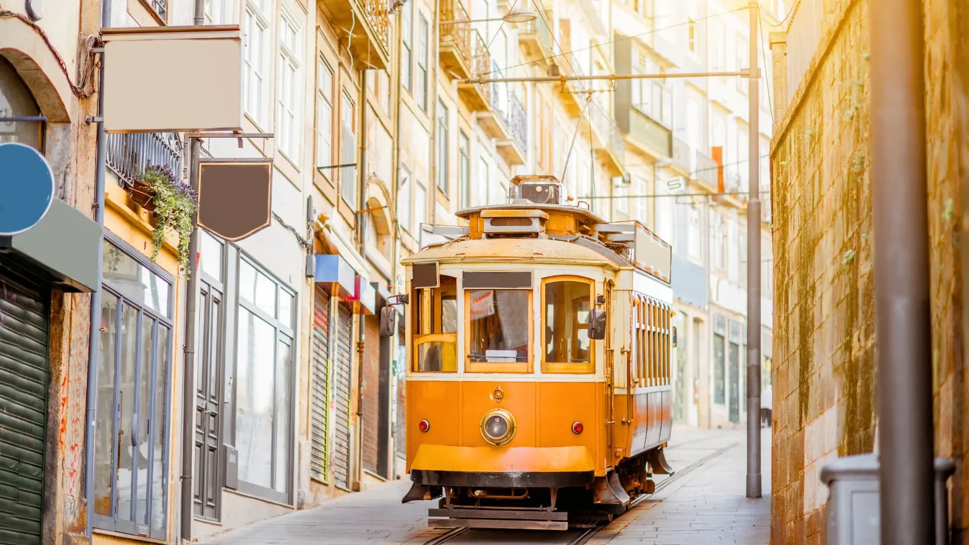 A vintage yellow Tram 28 passing through a narrow cobblestone street in Lisbon's Alfama neighborhood, with traditional Portuguese restaurants and cafés visible along the route