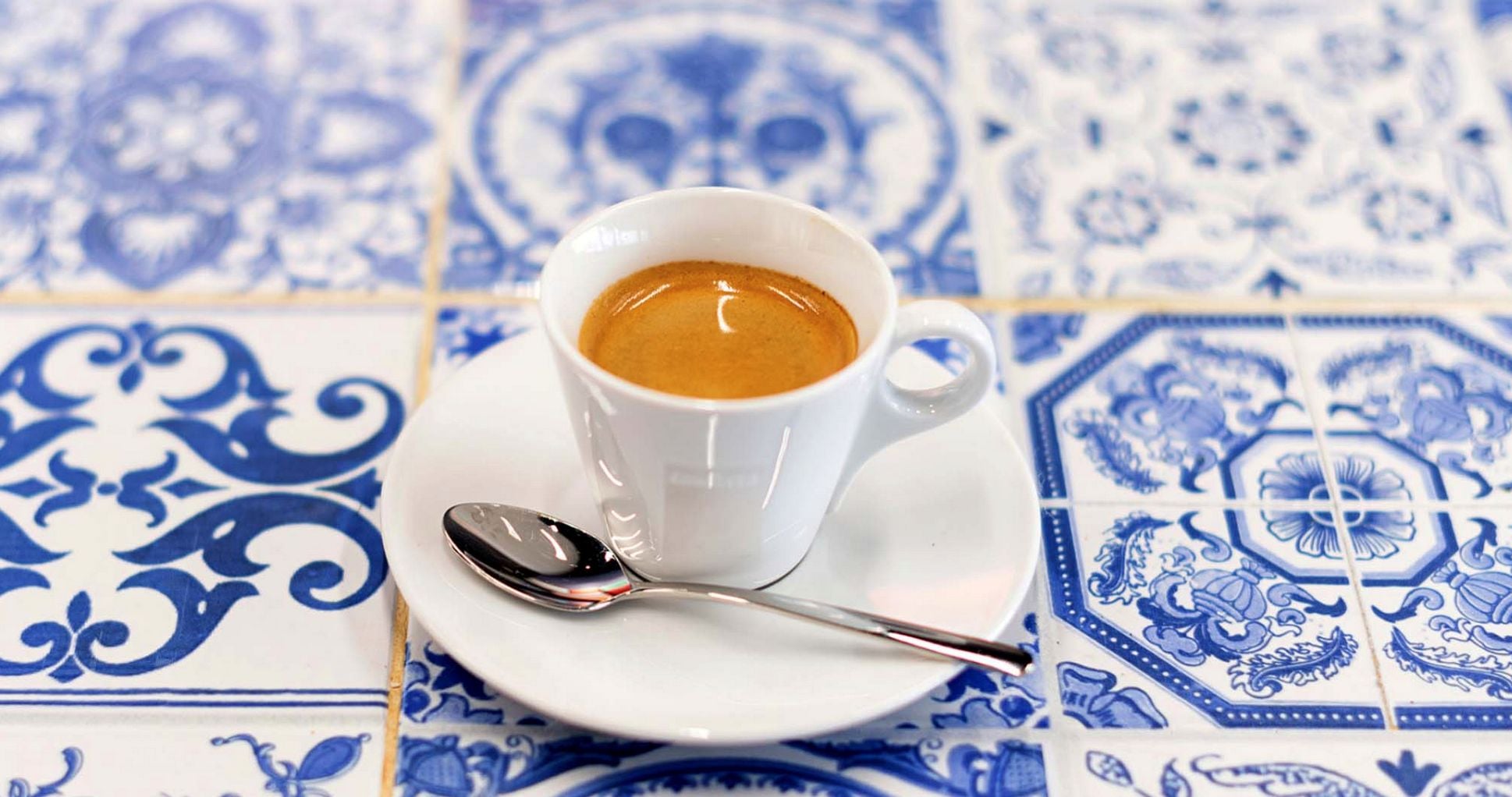 Traditional Portuguese coffee cups showing bica, meia de leite, and abatanado arranged on a marble café counter with vintage Portuguese coffee equipment in the background