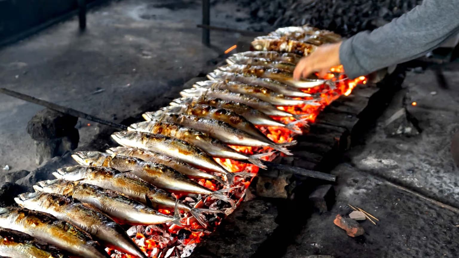 Grilled sardines sizzling on a charcoal grill during Santos Populares festival in Lisbon, with traditional Portuguese bread and roasted peppers alongside