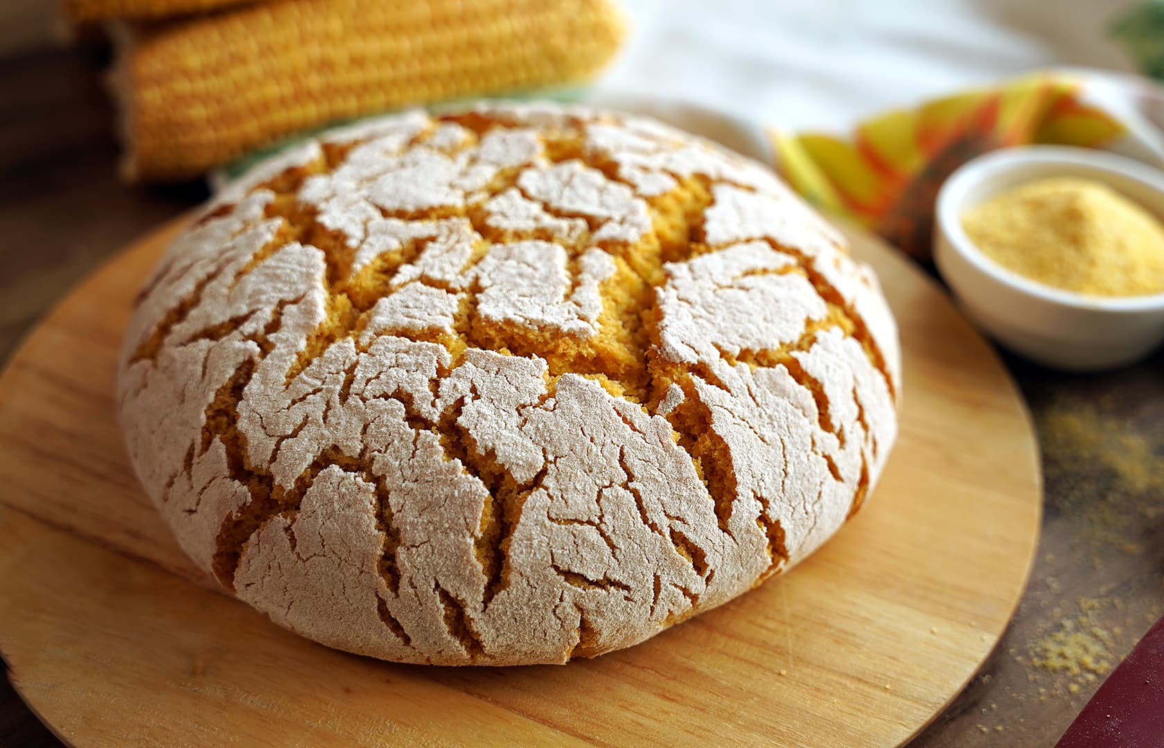Golden-crusted broa de milho bread with its characteristic cracked surface, displayed on a rustic wooden table with traditional Portuguese pottery and corn kernels scattered around